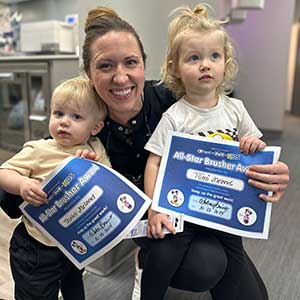 Dental professional with two toddlers holding certificates for a good visit